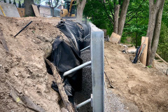 Galvanized steel I-beam soldier piles, helical pile anchors, and clear gravel backfill. Mississauga, Ontario.