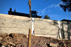 Excavator lowering precast concrete panels between steel I-beams. Burlington, Ontario.