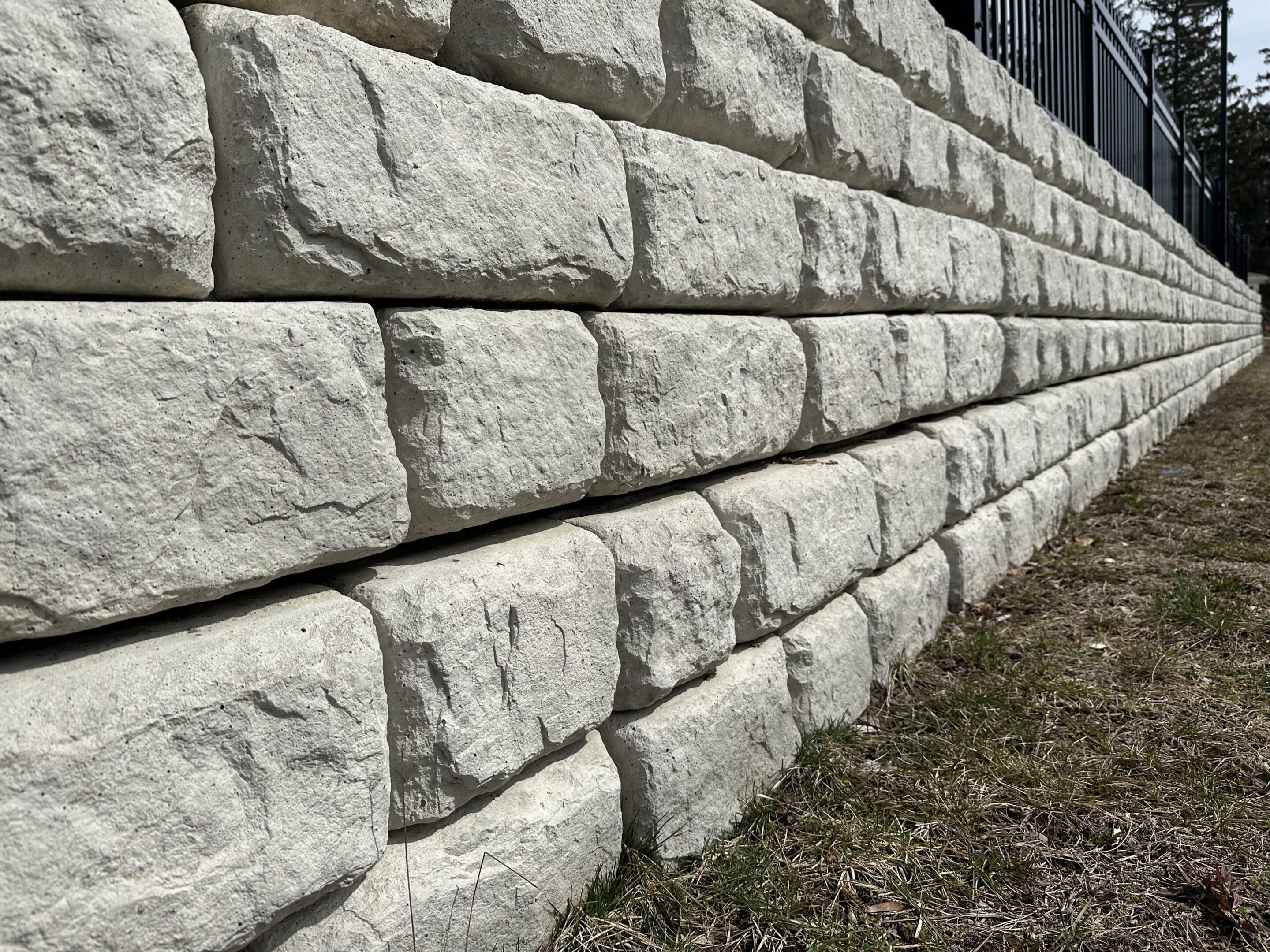Limestone retaining wall with grass and fence