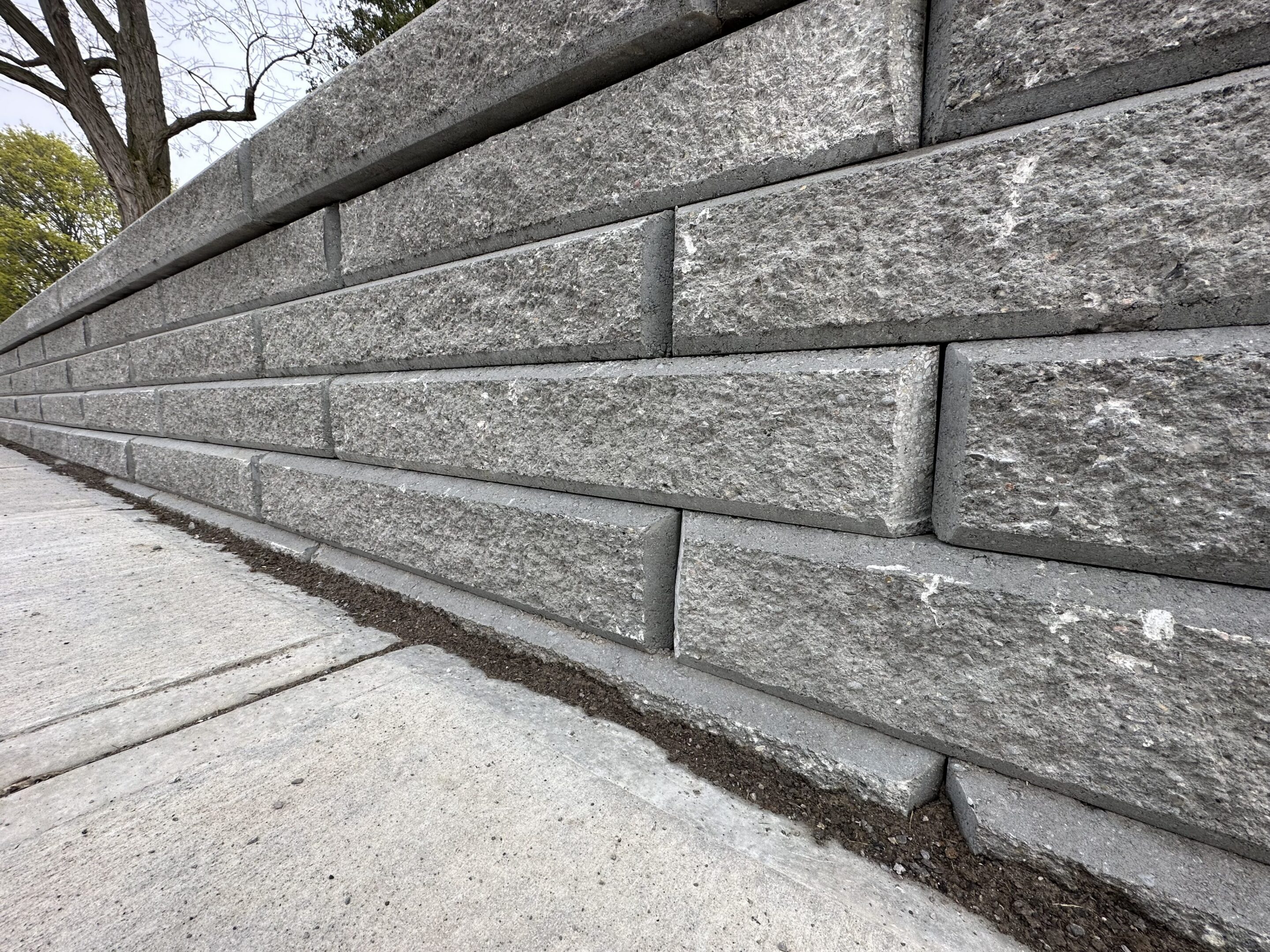 Gray stacked stone retaining wall beside sidewalk