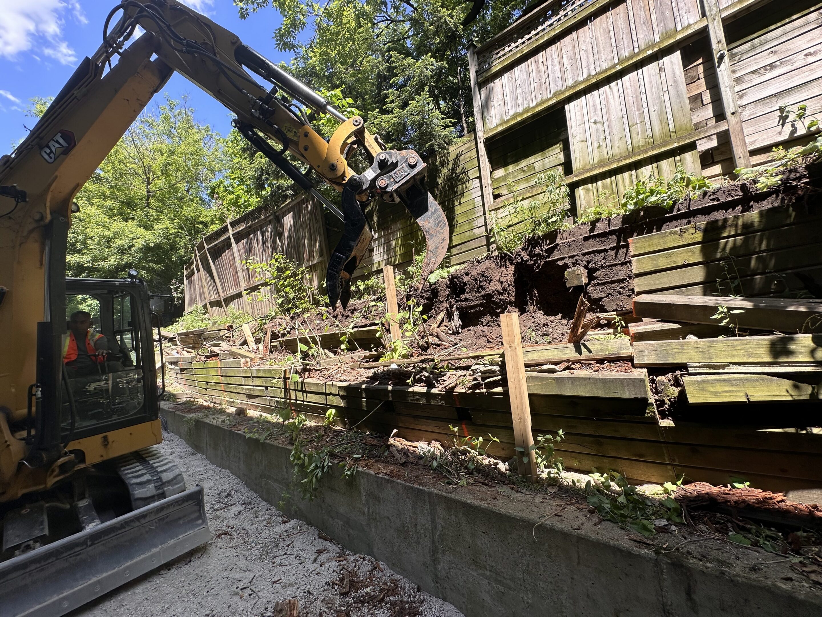 Excavator removing damaged wooden retaining wall